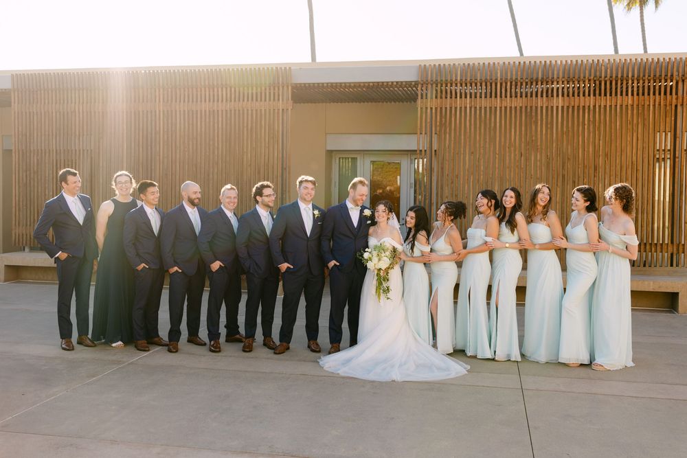 Wedding party in formal attire poses in line against wooden wall backdrop.