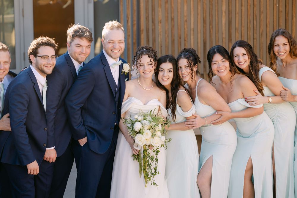 A wedding party poses together outdoors wearing formal attire in white and navy blue colors.