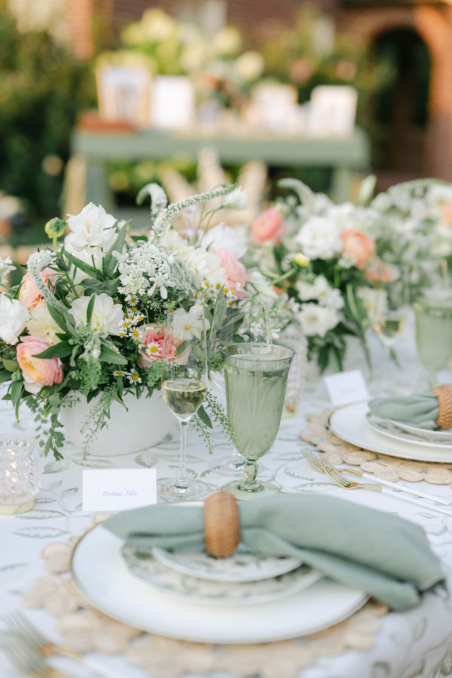 Elegant table setting with white plates, gold flatware, and woven placemats adorned with coral and white floral arrangements. - Elawa Farm