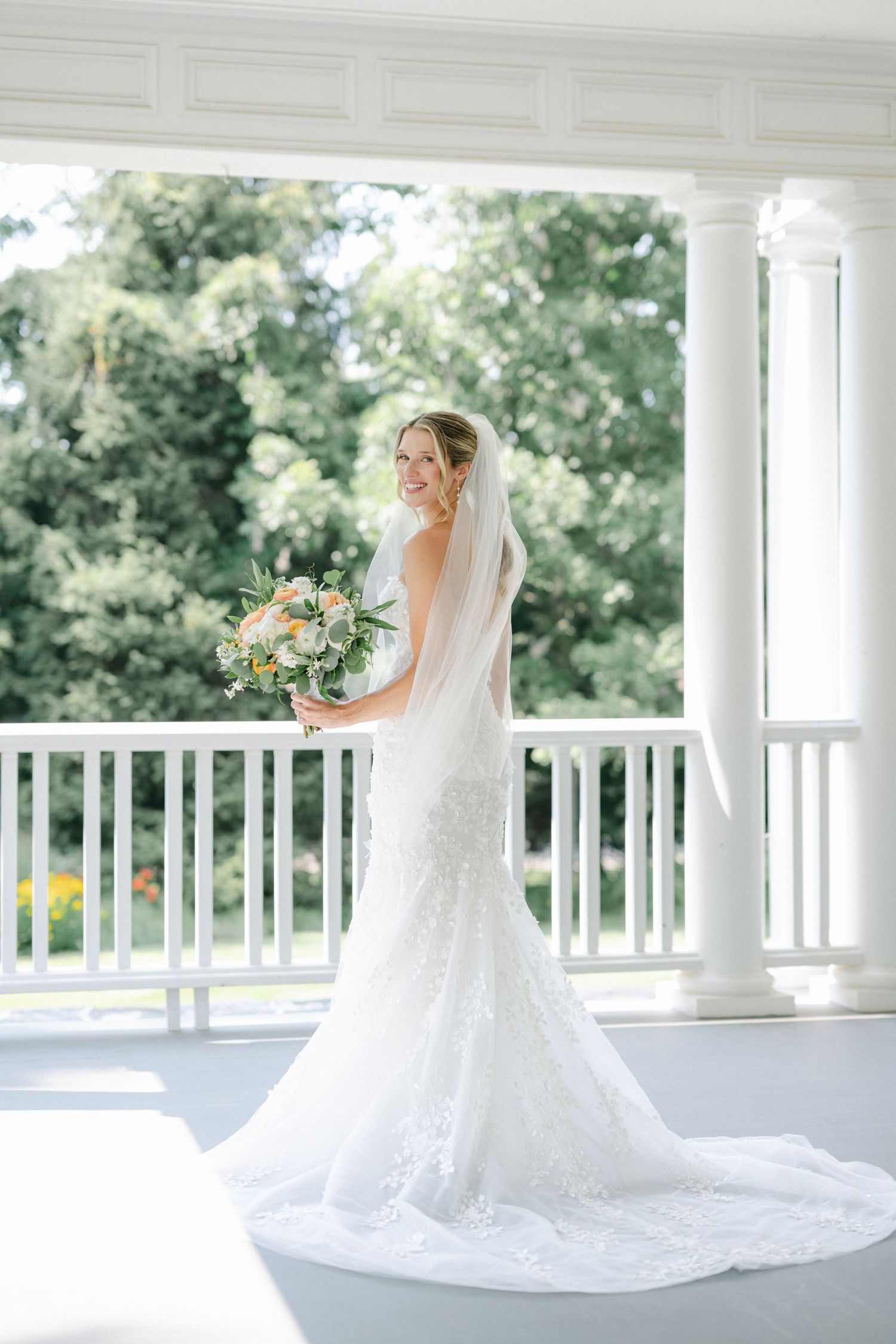 A bride in a white strapless gown holds a peach and white bouquet while wearing a veil against a soft bokeh background. - Lake Forest