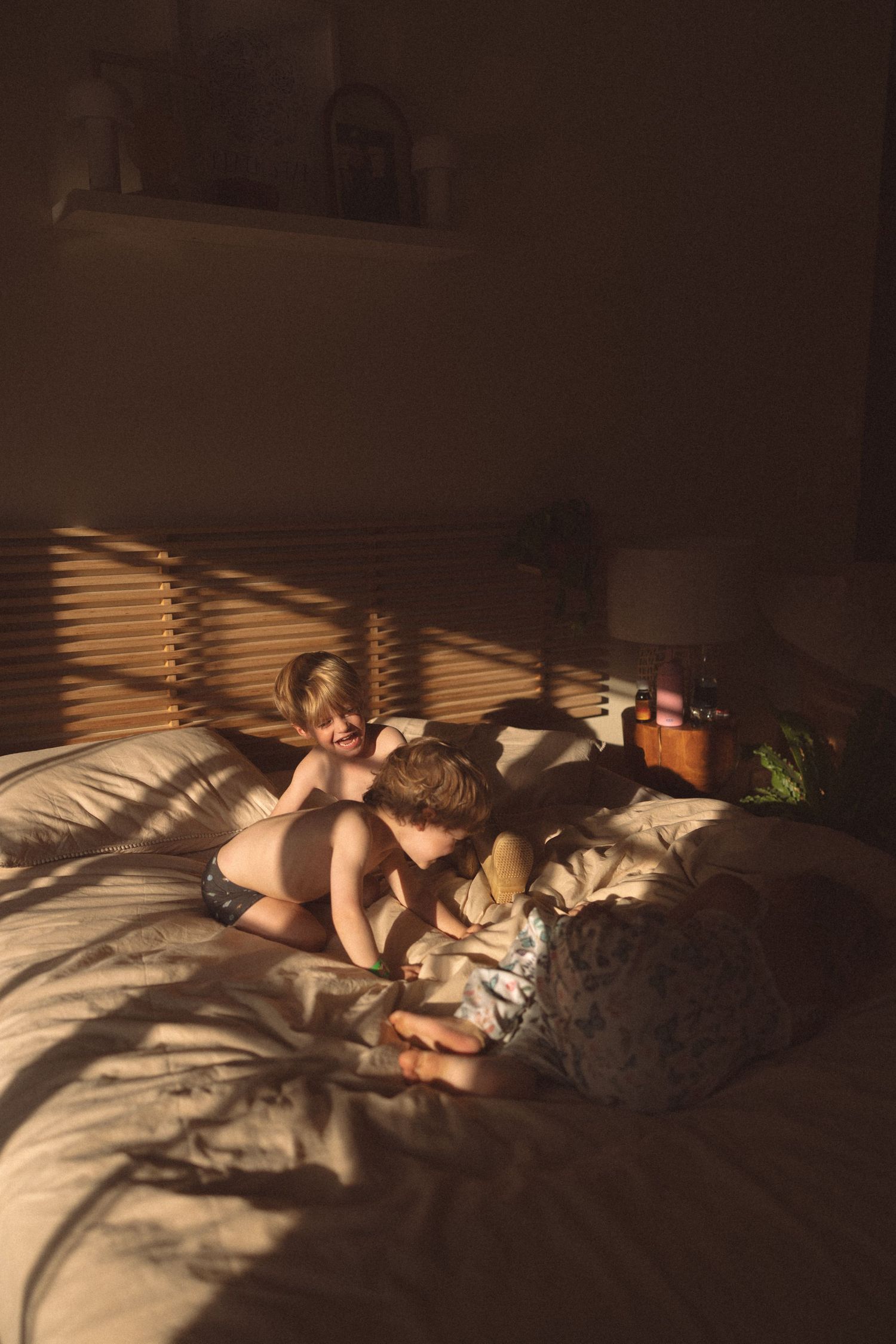A child sleeps peacefully on a bed with sunlight streaming through window blinds creating dramatic shadows.