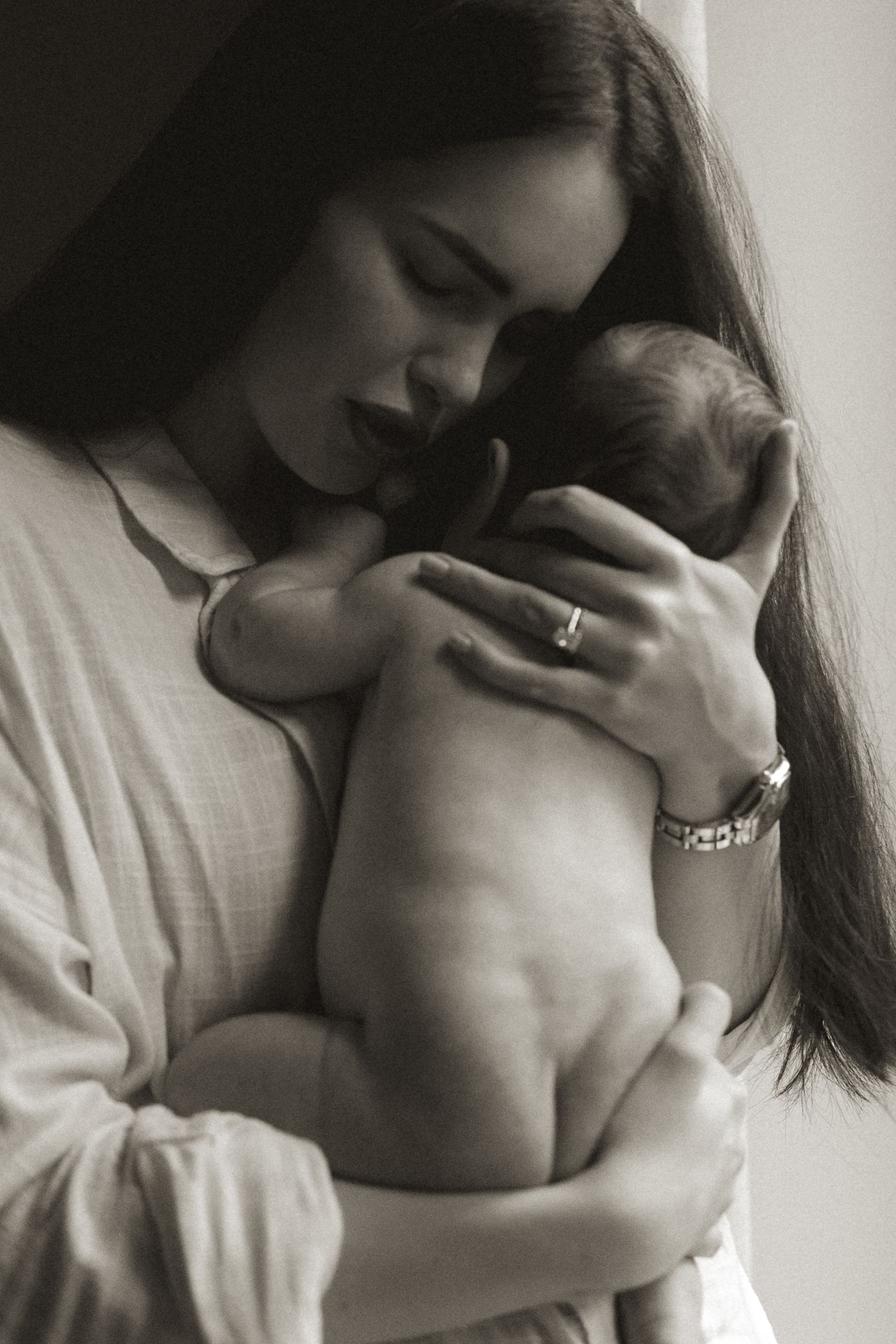 Black and white photo of a young mother tenderly cradling her newborn baby close to her face.