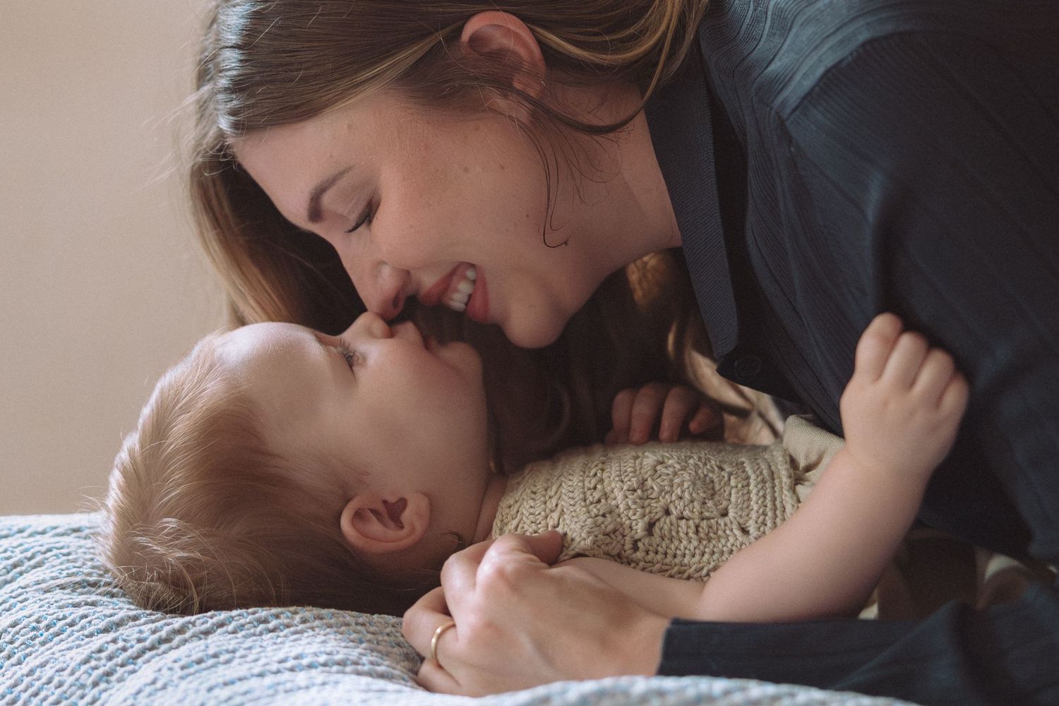A loving mother smiling and cuddling her happy baby on a soft blue blanket in a tender moment.