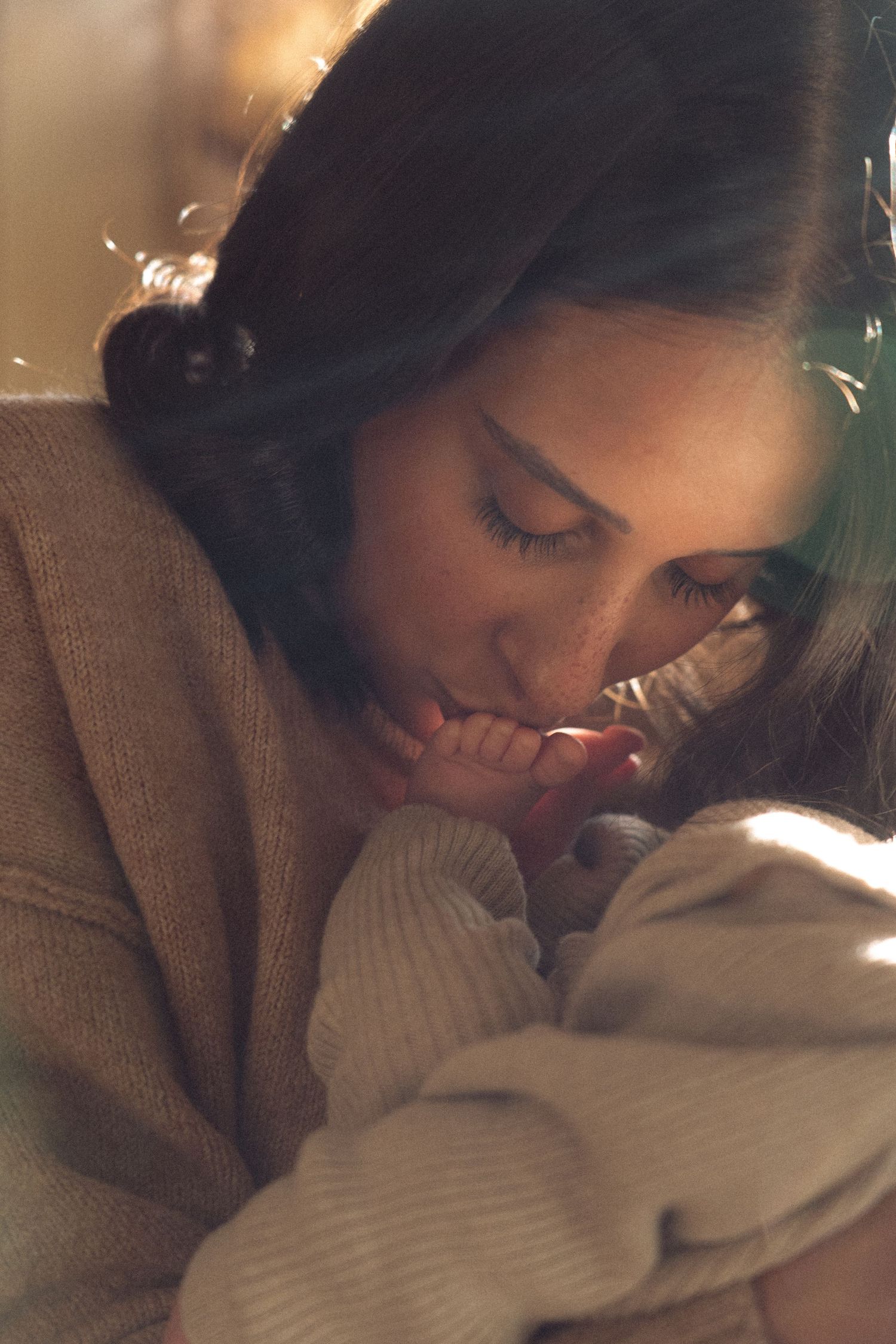 A person in a brown sweater leans down to cuddle with a small white dog in a warm, intimate moment.