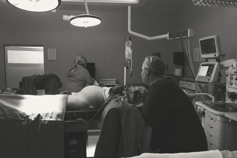 Medical staff work in a dimly lit hospital room with monitoring equipment and computers visible.