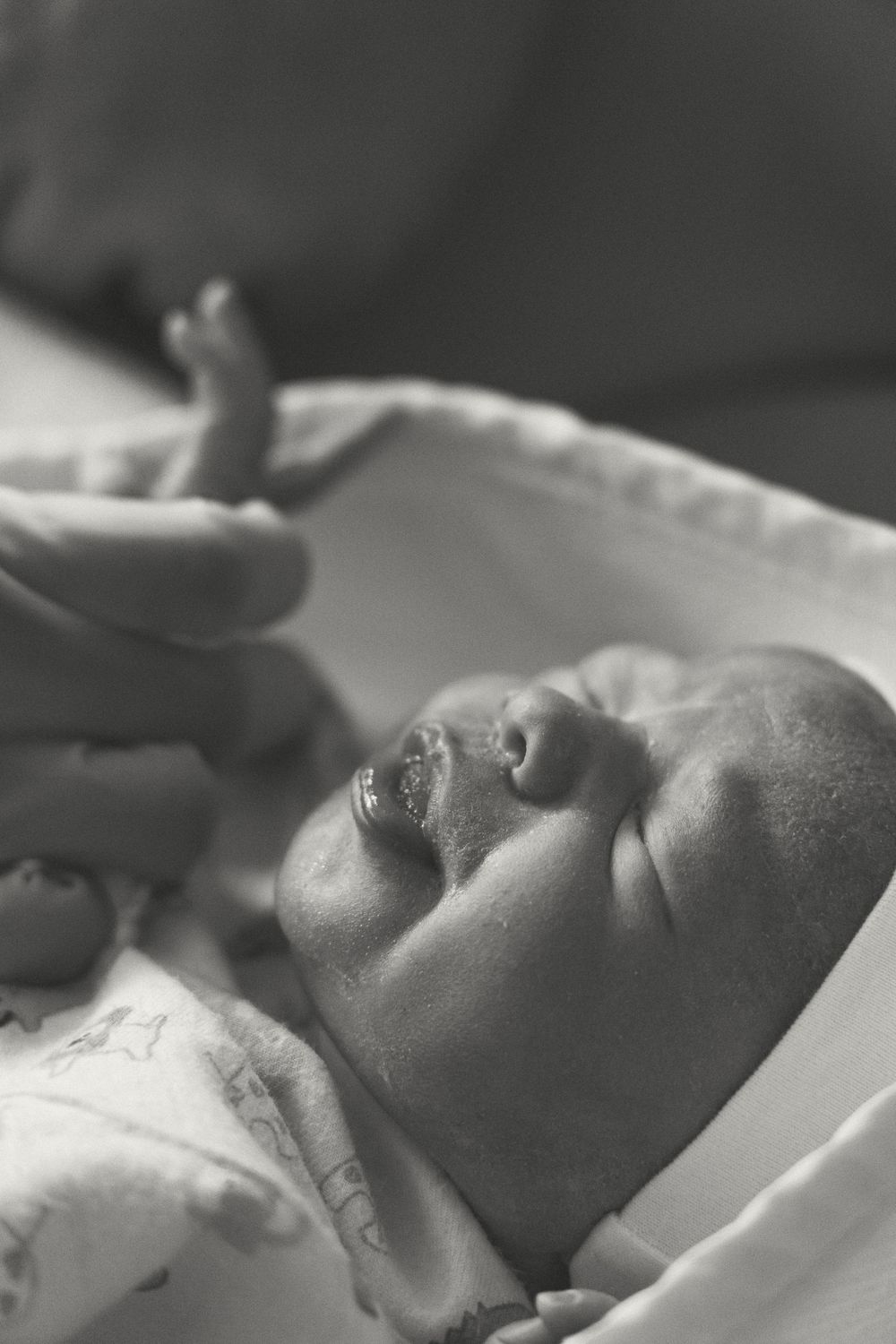 A peaceful black and white photograph of a sleeping baby swaddled in soft white fabric.