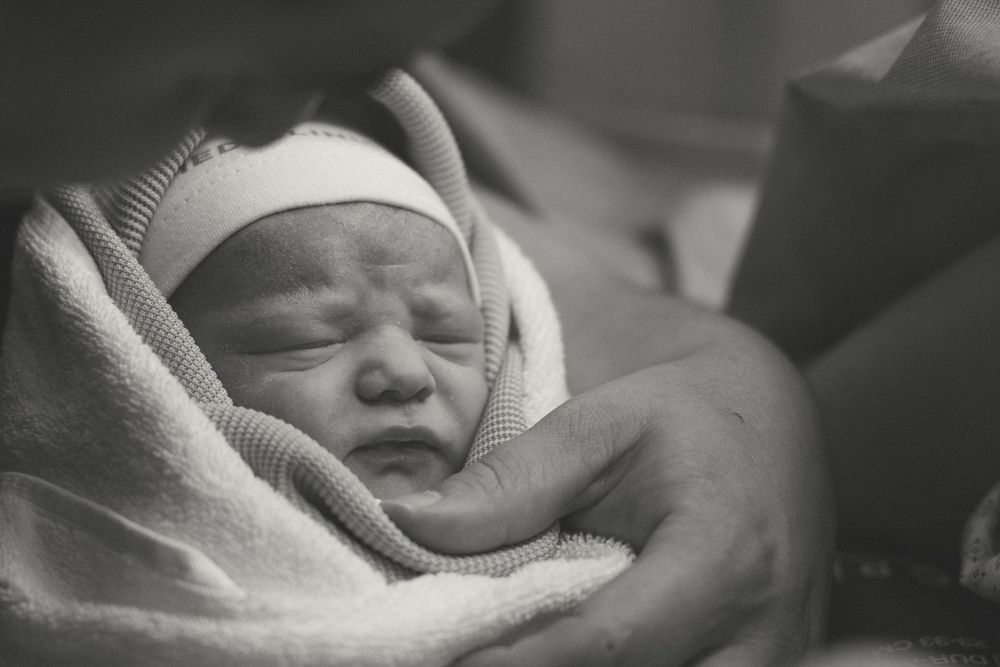 Newborn baby wrapped in white blanket sleeping peacefully in black and white photograph.