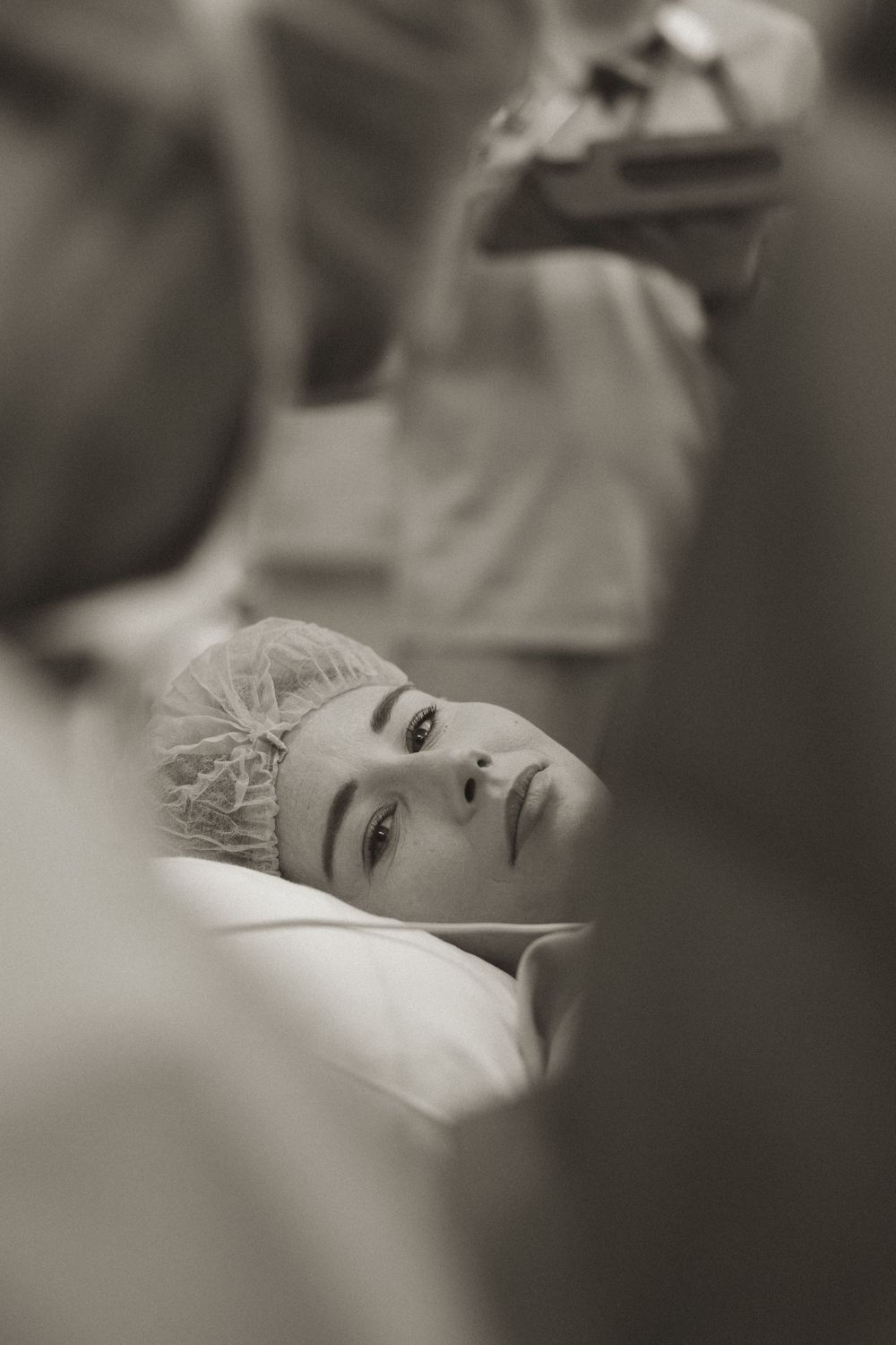 A patient wearing a surgical cap lies on a hospital bed in a black and white photograph.
