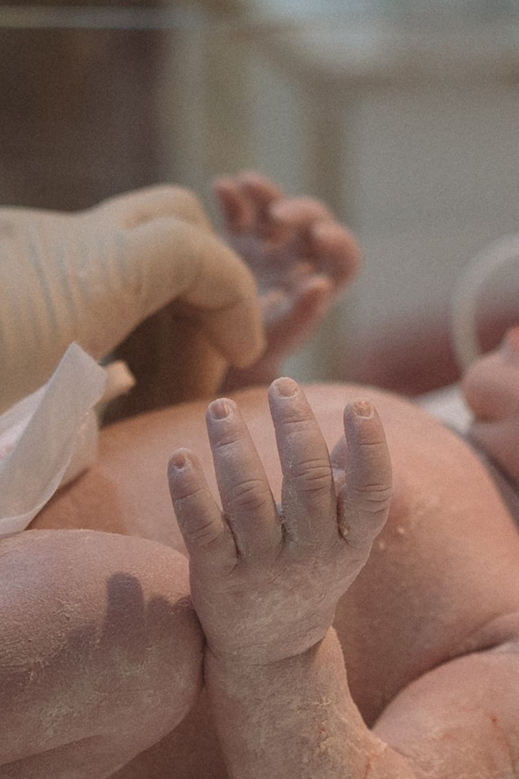 A close-up view of a newborn baby's tiny fingers reaching up against a soft, blurred background.