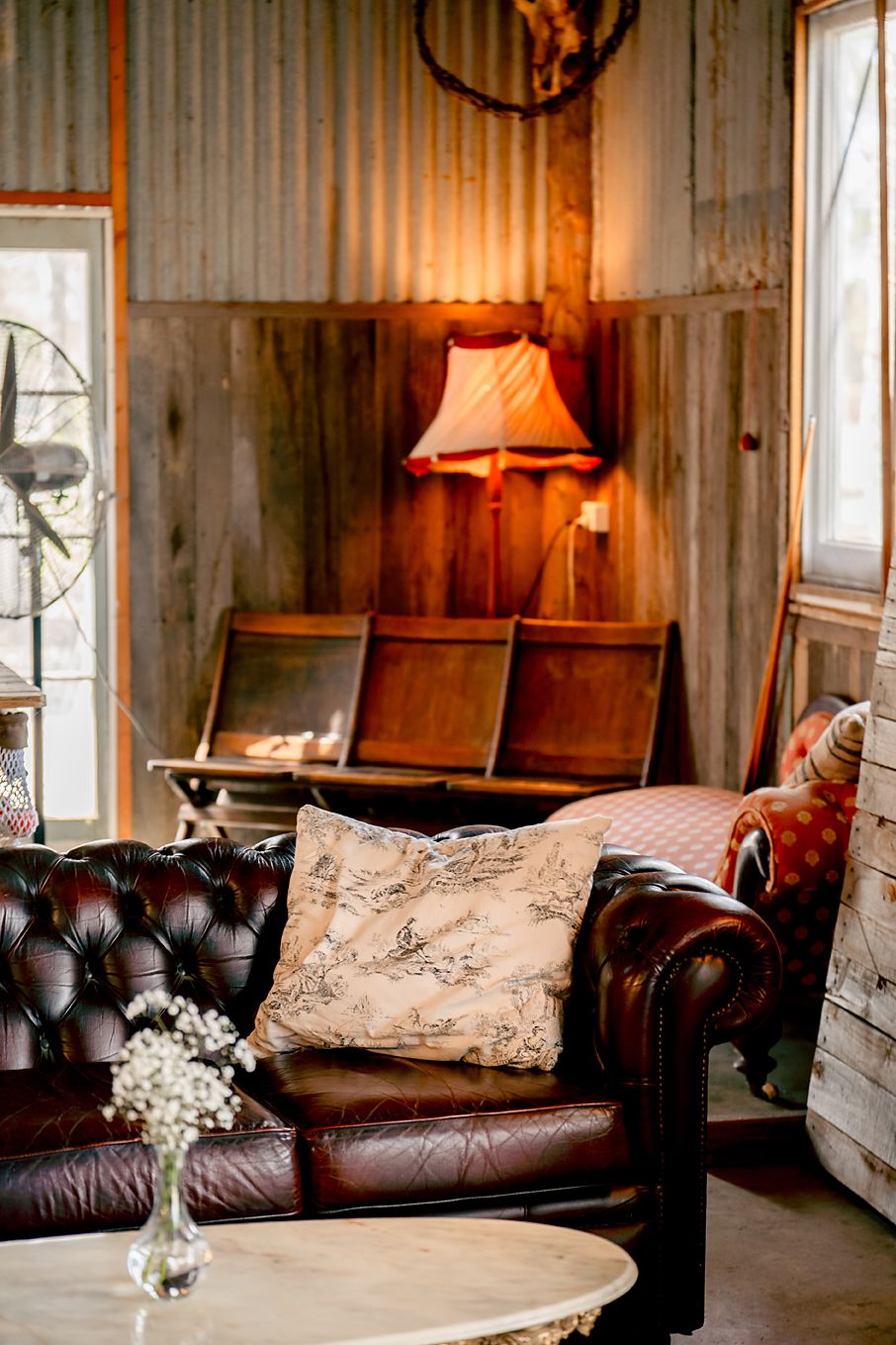 Vintage-style lounge area with brown leather couch, decorative pillows, and soft lighting in a rustic wooden interior.