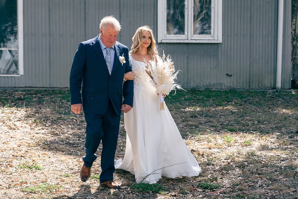 A couple in wedding attire walks together through a sunlit outdoor setting during their special day.