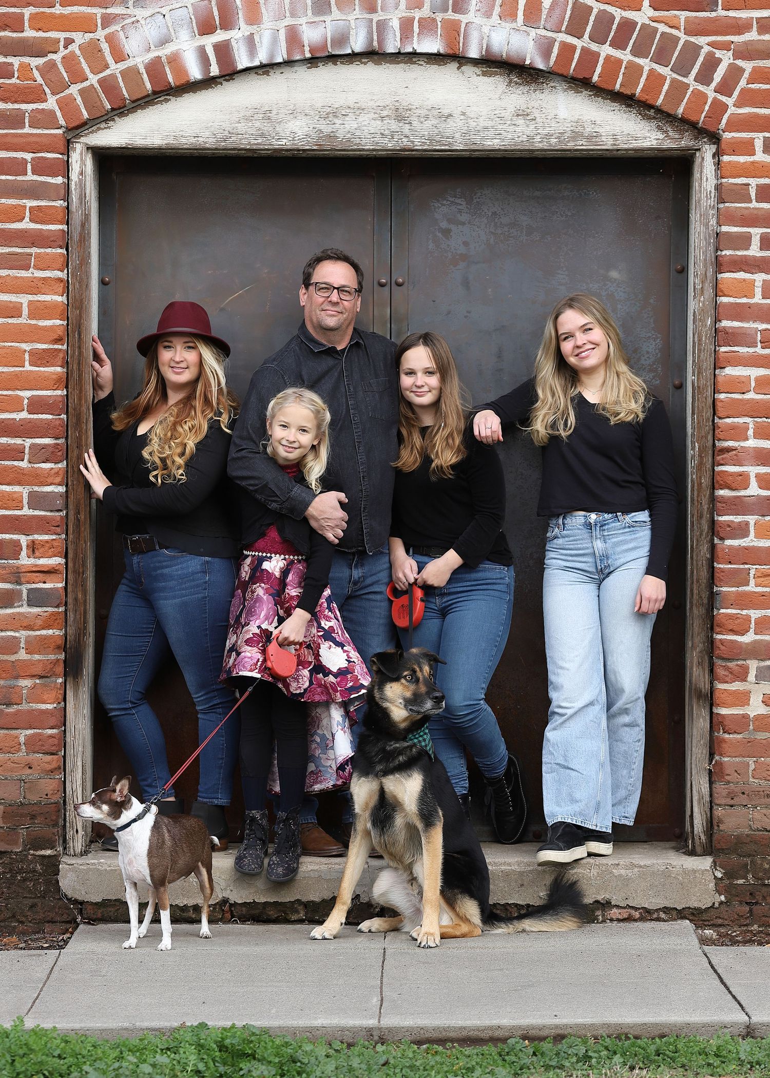 A group poses with dogs in a brick doorway while taking a series of casual family photos.