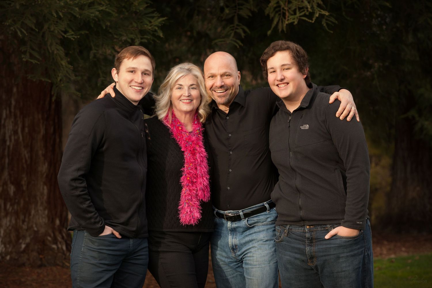 A group of people in dark clothing and jeans pose together outdoors against a dark background.