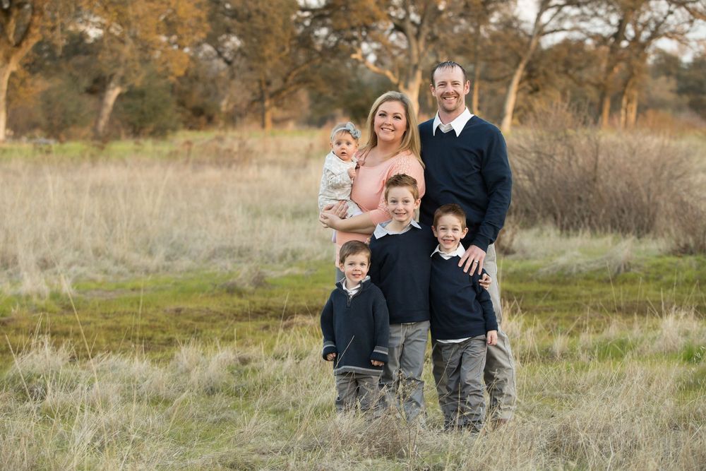 Family portrait session outdoors in a natural field setting with tall grass and autumn colors in the background.