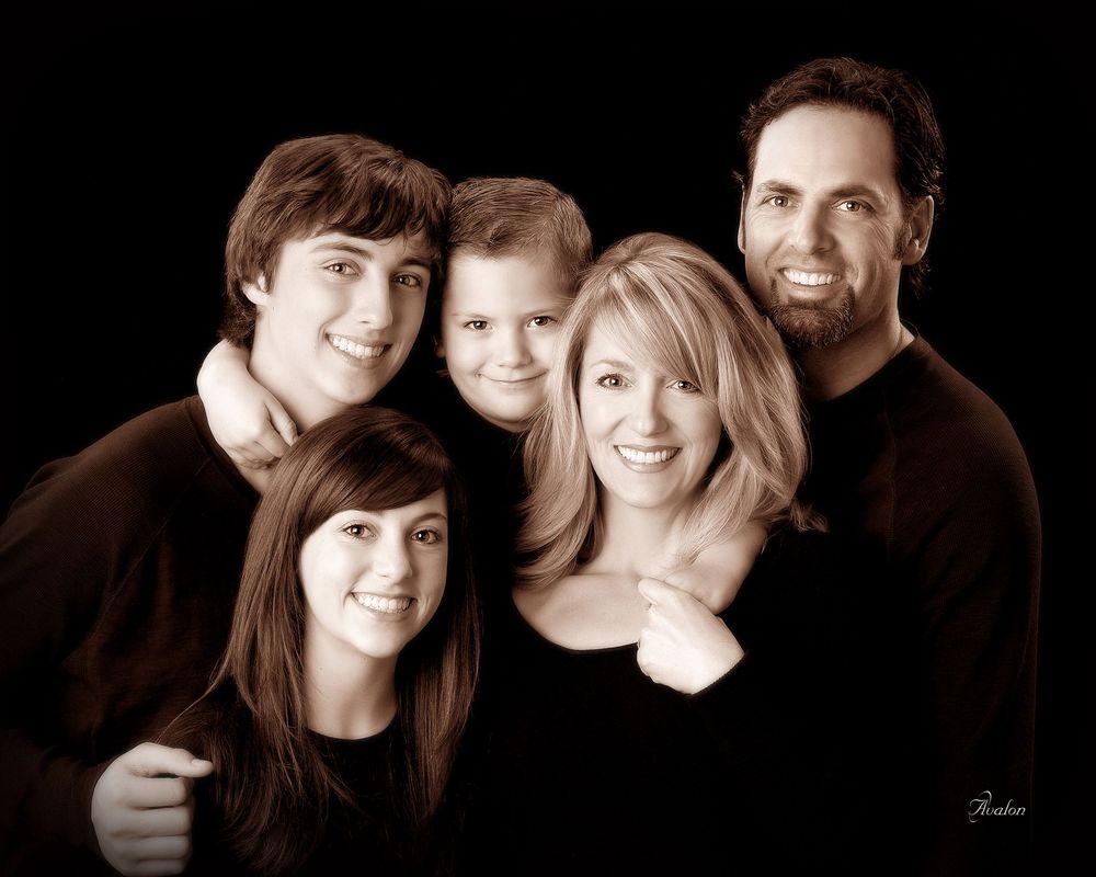 A series of seven black and white studio portraits showing intimate family moments against dark backgrounds.