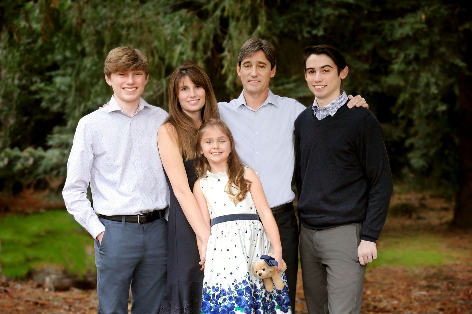 A group of young people in formal attire pose together outdoors in a garden setting for portraits.