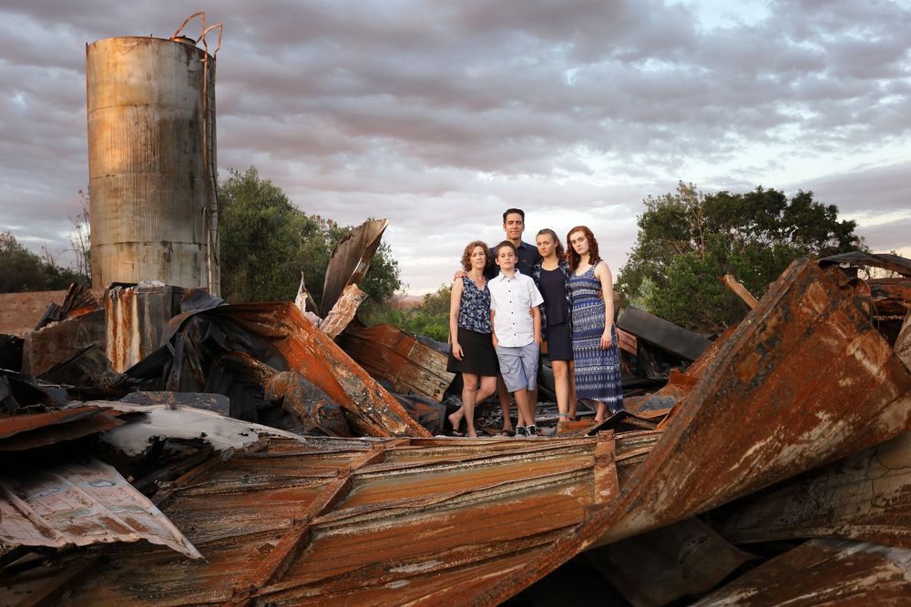 Storm damaged metal debris and wreckage scattered near a tall silo structure at sunset.