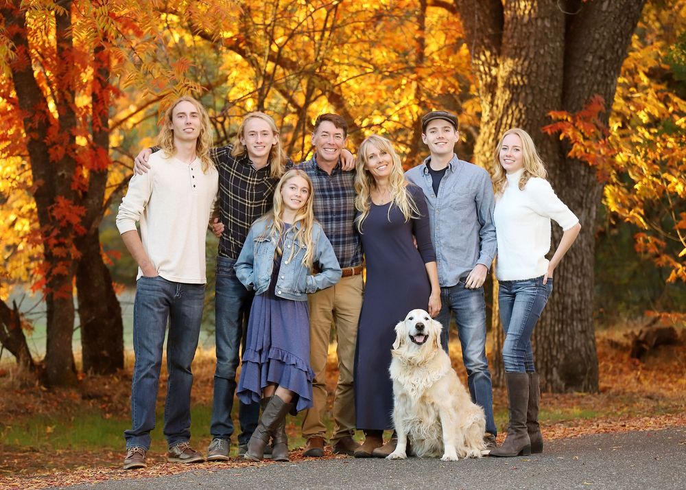 A group stands together with their golden retriever dog against vibrant autumn foliage in a park setting.