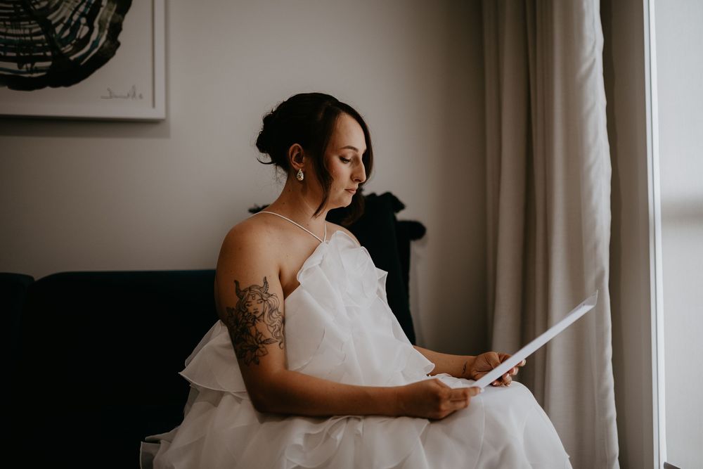 A white wedding dress hangs by a window in soft natural light.