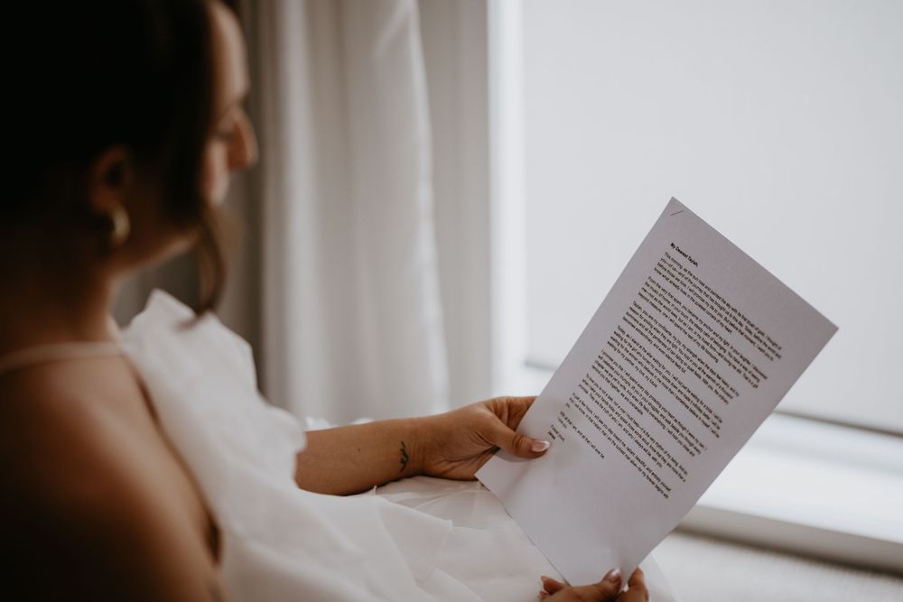 Close-up shot of hands holding wedding ceremony program or vows on white paper.
