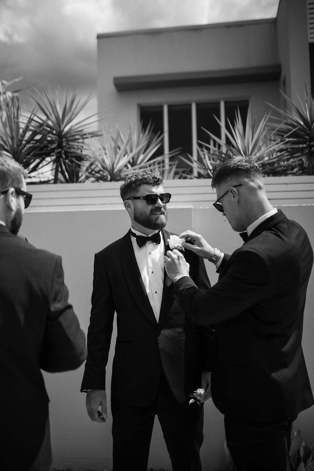 Men in formal black tuxedos and bow ties preparing for a special event outdoors.