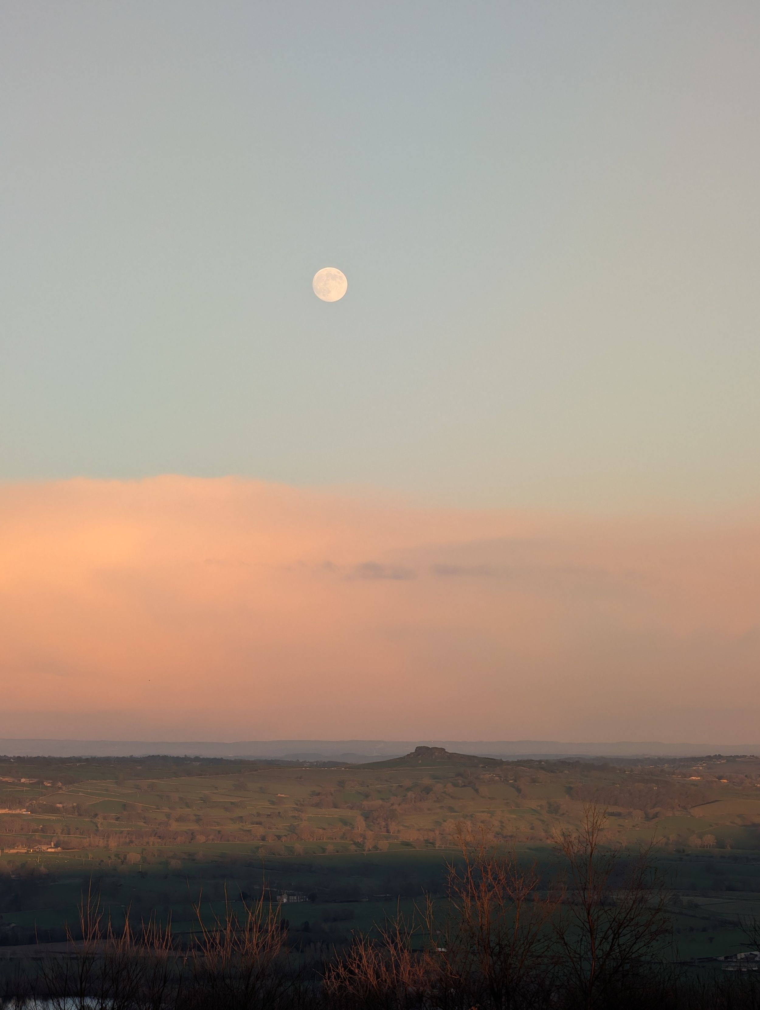 A full moon rises over a desert landscape at dusk with warm orange and pink hues in the sky.