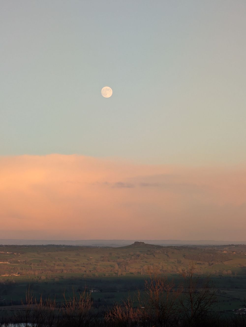 A full moon rises over a desert landscape at dusk with warm orange and pink hues in the sky.