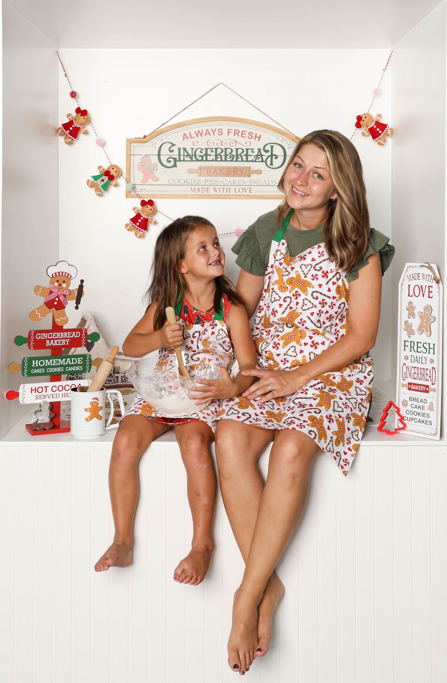 Two people wearing matching floral dresses pose playfully in a white studio setting with holiday decorations. Box photography session