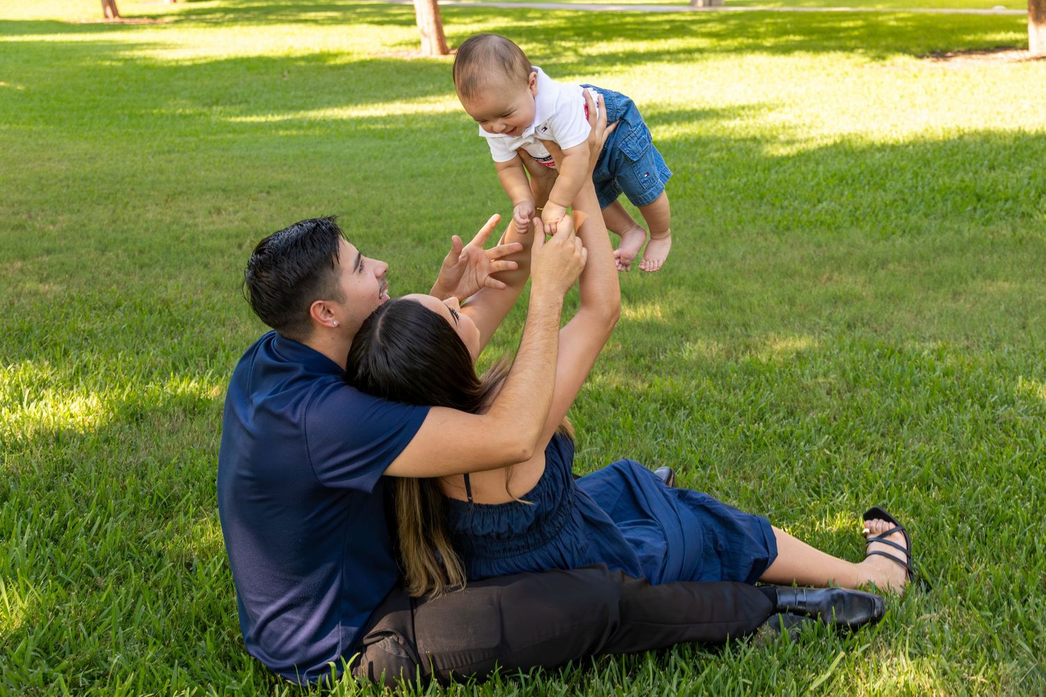 A parent and baby playing together on green grass in a sunny park on a summer day.