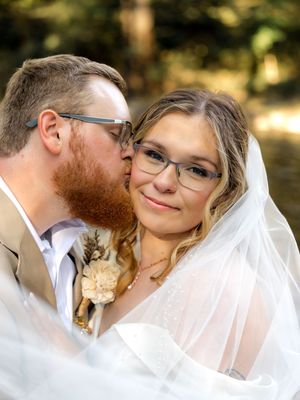 A couple shares tender moments in their wedding attire against a sunlit outdoor backdrop.