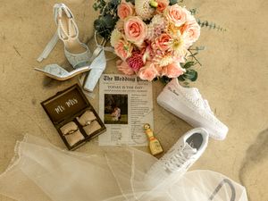 Vintage wedding details with pink roses, antique books, white lace boots, and old documents on textured beige background.