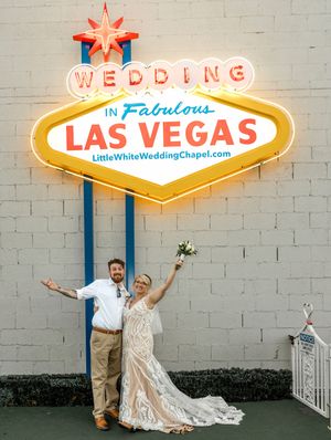 A couple celebrates under the iconic neon Las Vegas Wedding Chapel sign against a white wall.