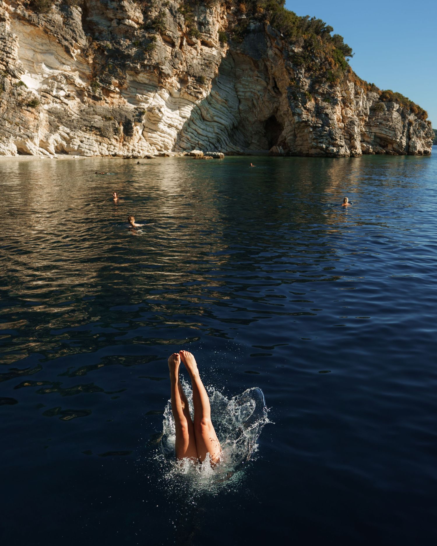 A sequence of cliff diving shots showing feet emerging from blue Mediterranean waters against a rocky coastline.