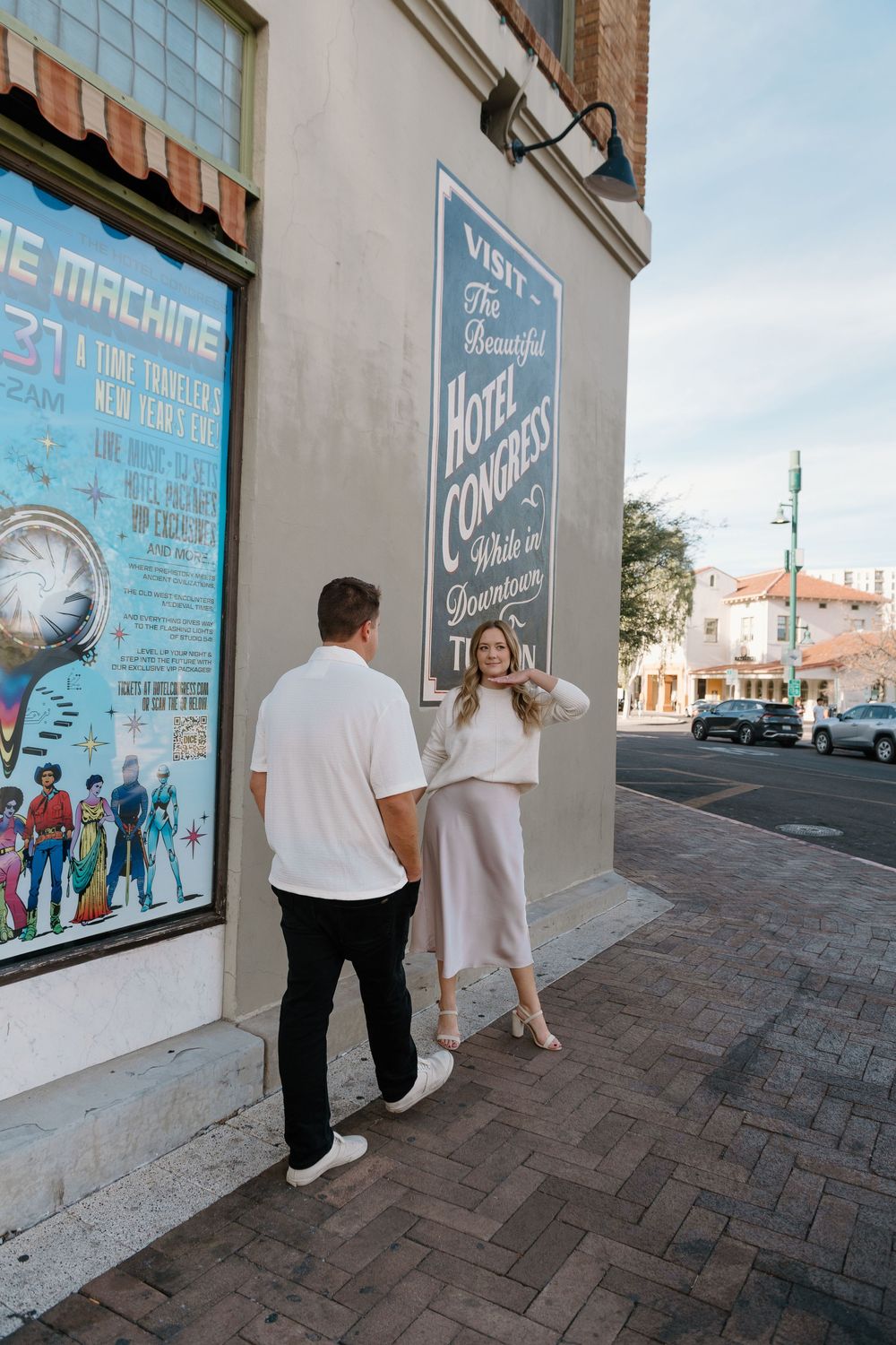 People viewing colorful posters and artwork displayed on exterior building wall along brick sidewalk.