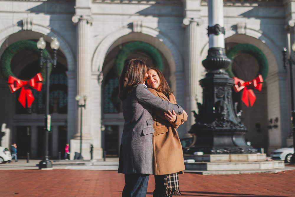 Couple embracing while standing in front of an ornate stone building with arches and holiday decorations at the Union Station DC