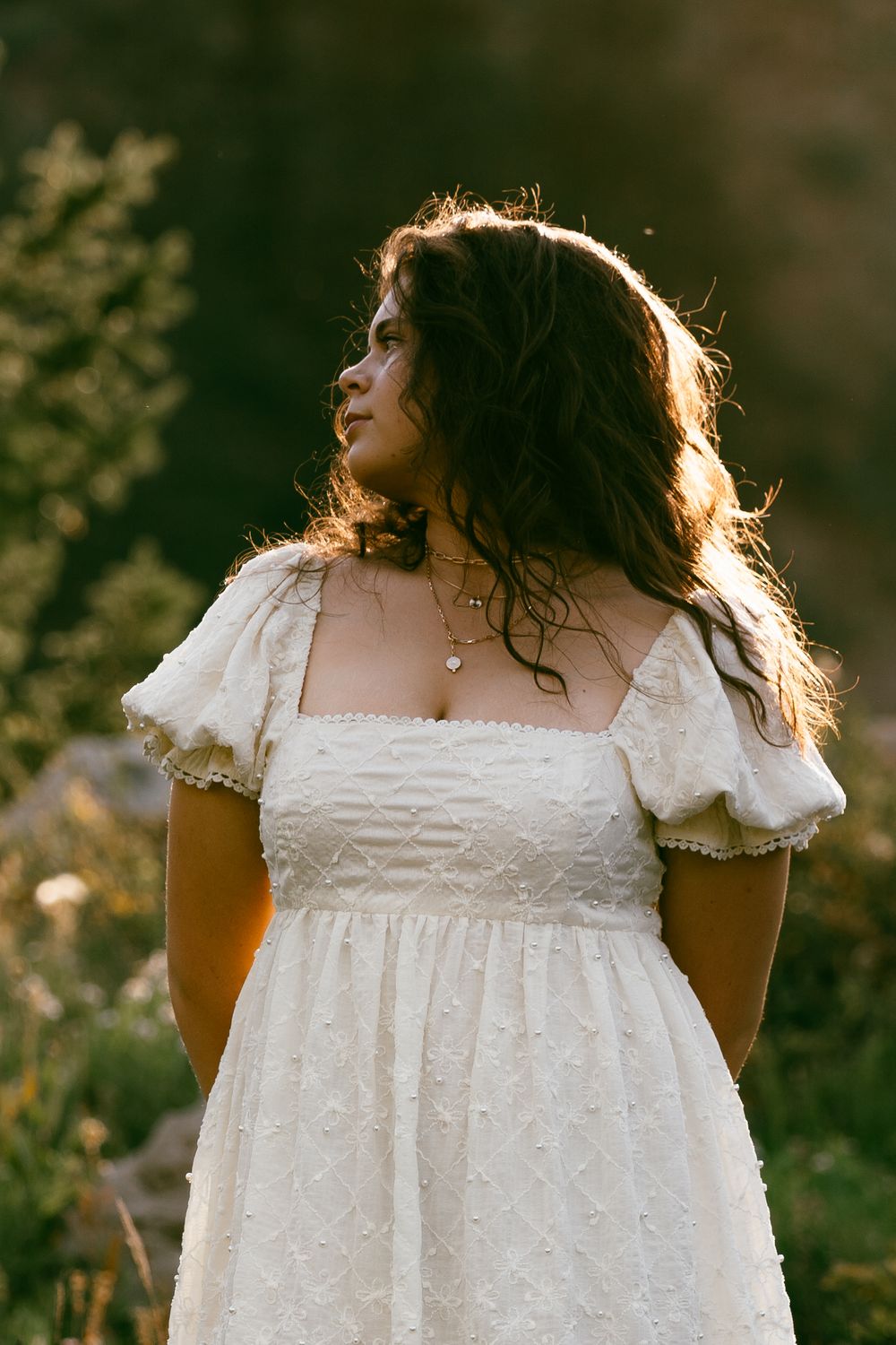 A white cotton dress with delicate lace trim and puff sleeves is shown in a warm sunset glow.