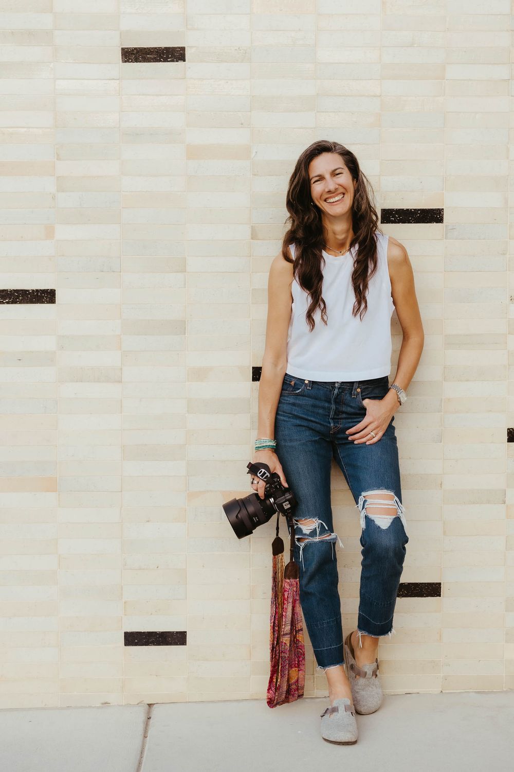 Person in casual attire sitting against textured stone wall with camera.