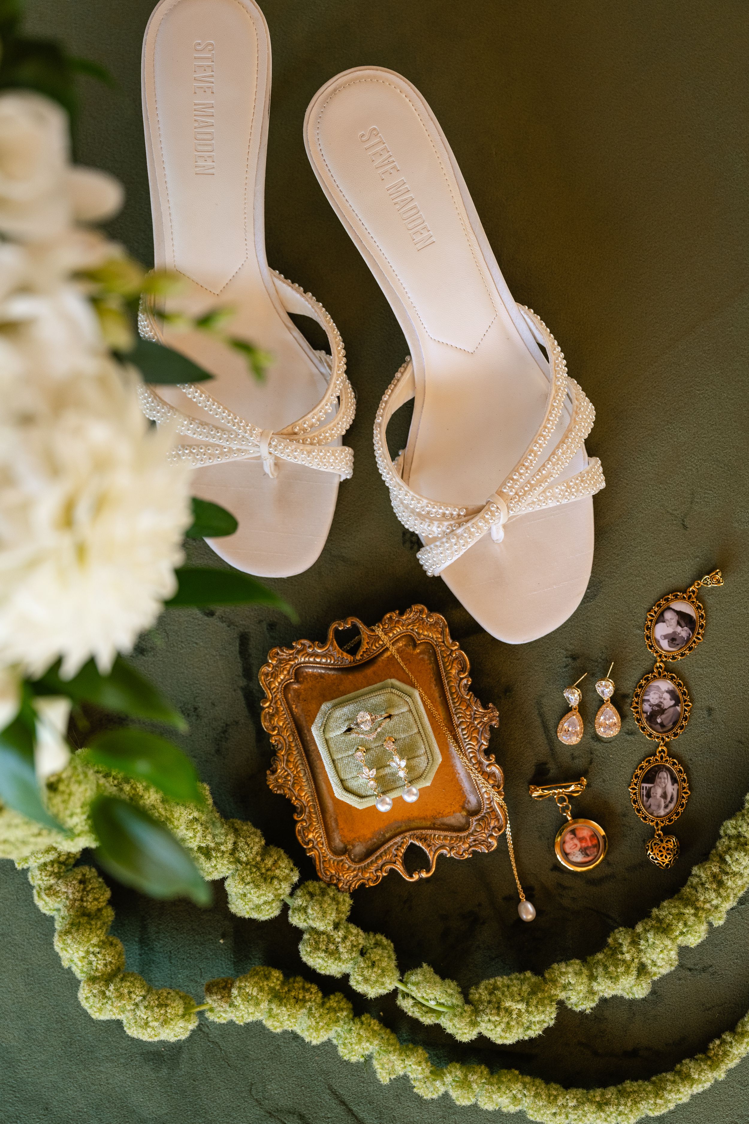 Elegant bridal accessories including white heels, vintage-style cameo jewelry, and earrings arranged with white flowers.