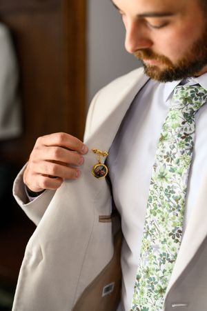 Groom in light gray suit with floral tie adjusts his boutonniere in a series of detail shots.