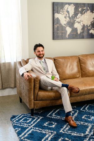 A person in a light suit relaxes on a brown leather couch with a blue patterned rug and world map wall art.