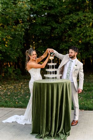 A couple playfully feeds each other wedding cake at their outdoor reception with a green velvet tablecloth.