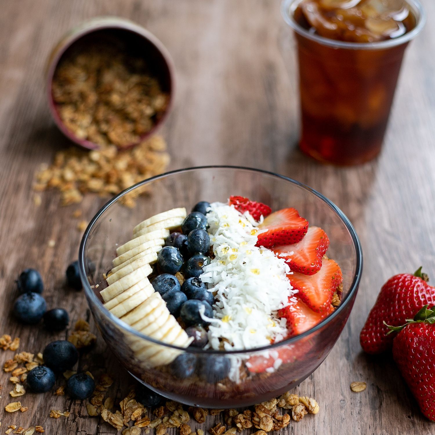 Fresh acai bowl topped with berries, coconut flakes and granola on rustic wooden table.