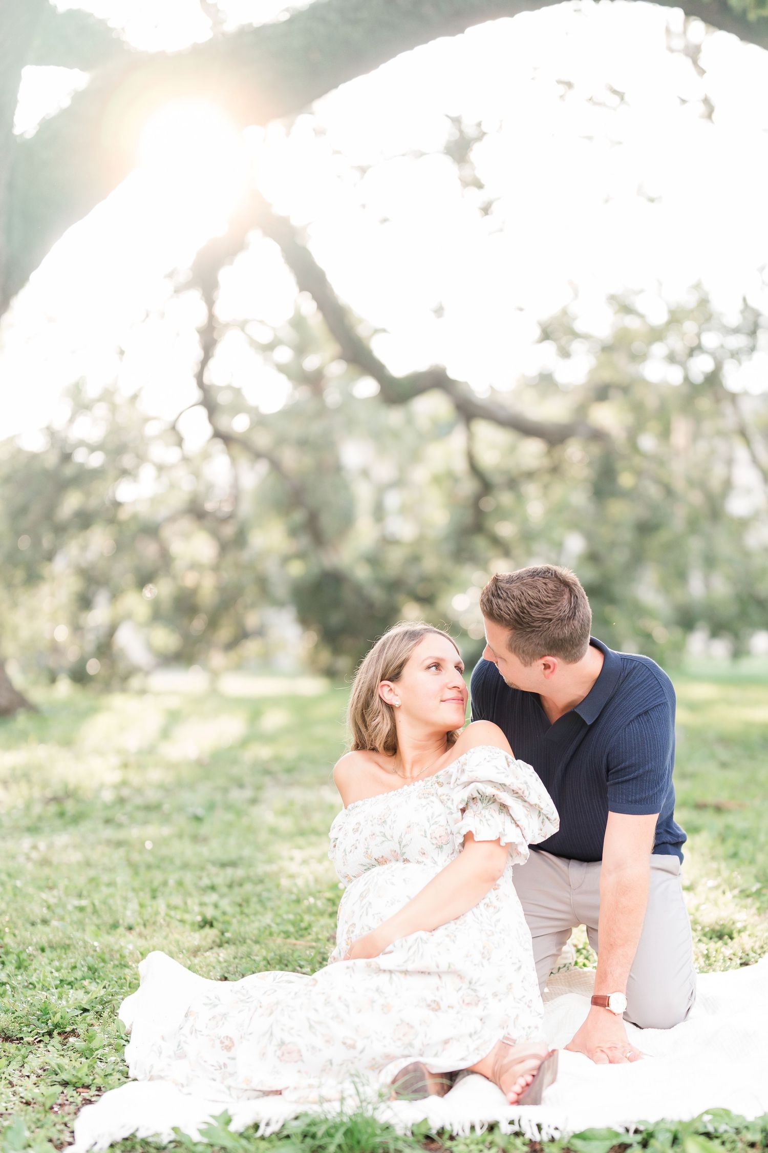 Expectant couple shares tender moments in a field of pink muhly grass during sunset maternity photoshoot.