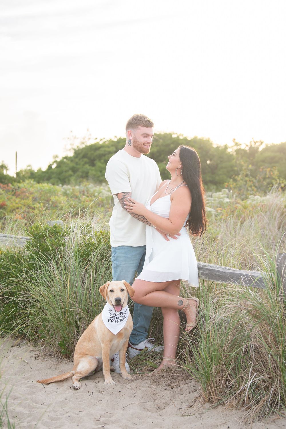 Happy couple with their lab dog posing on sandy coastal path.