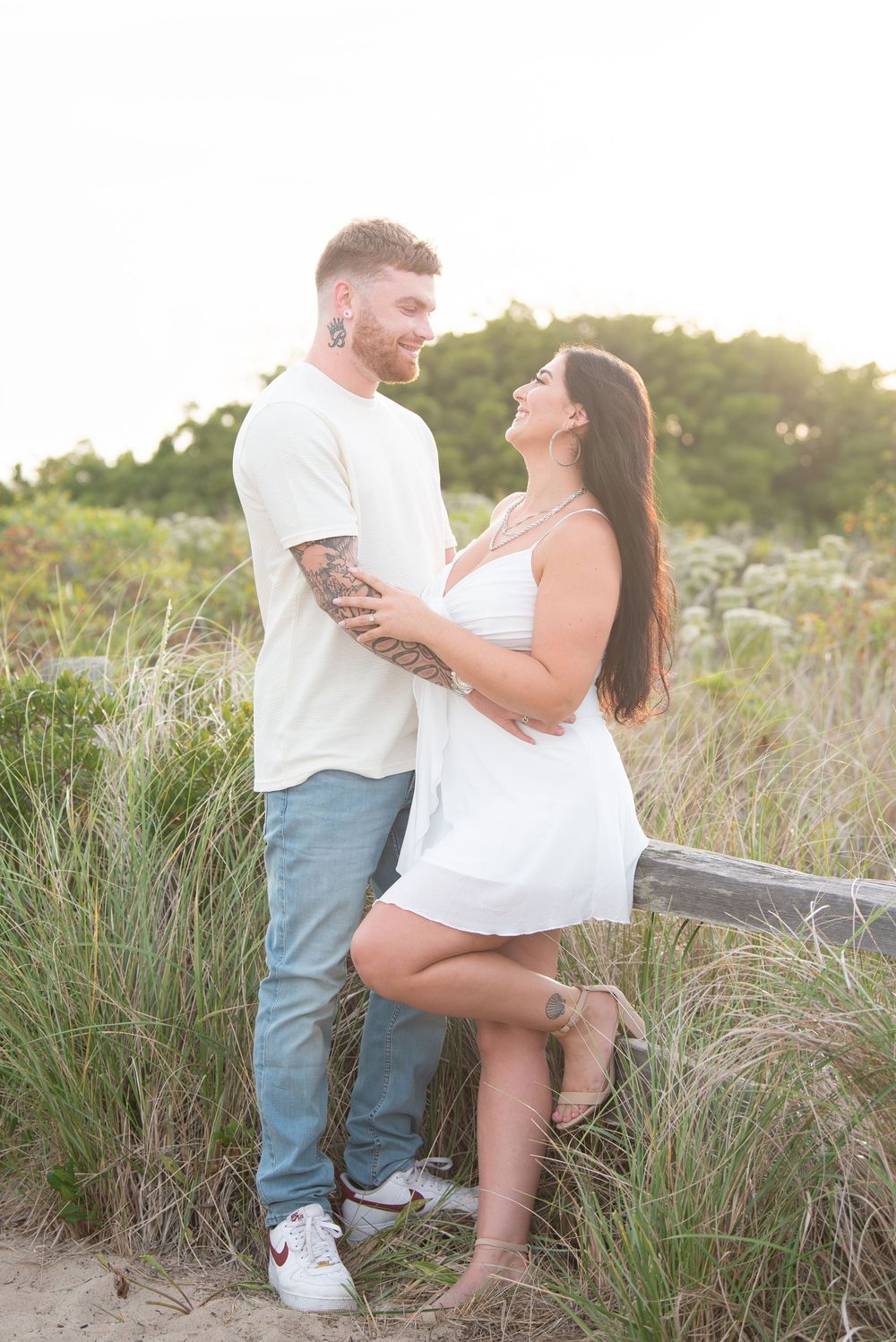 Couple embracing on wooden fence along beach path at sunset.