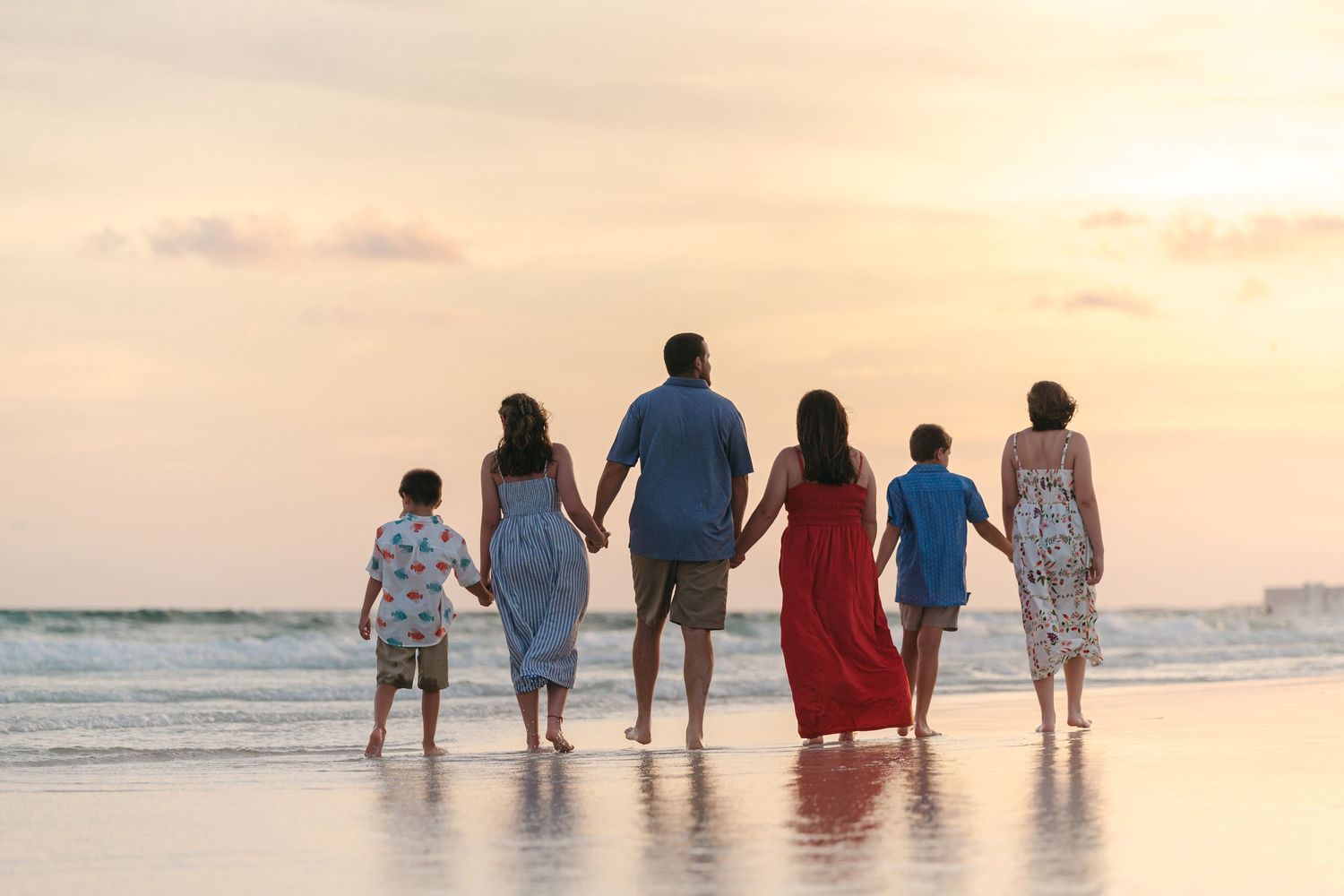 A group of people walk together in shallow ocean water at sunset creating a peaceful beach scene.