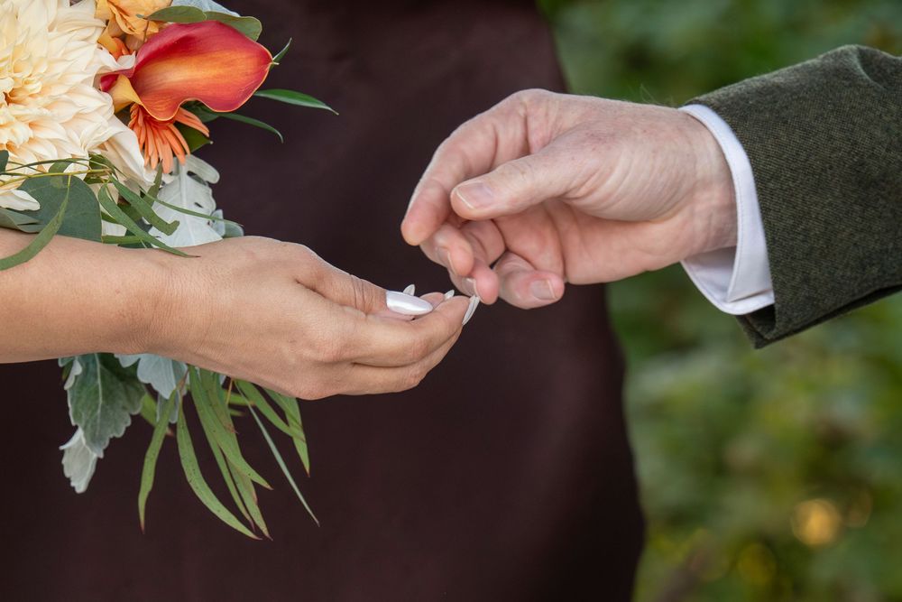 A couple holding hands during an outdoor wedding ceremony with peach and white floral arrangements.