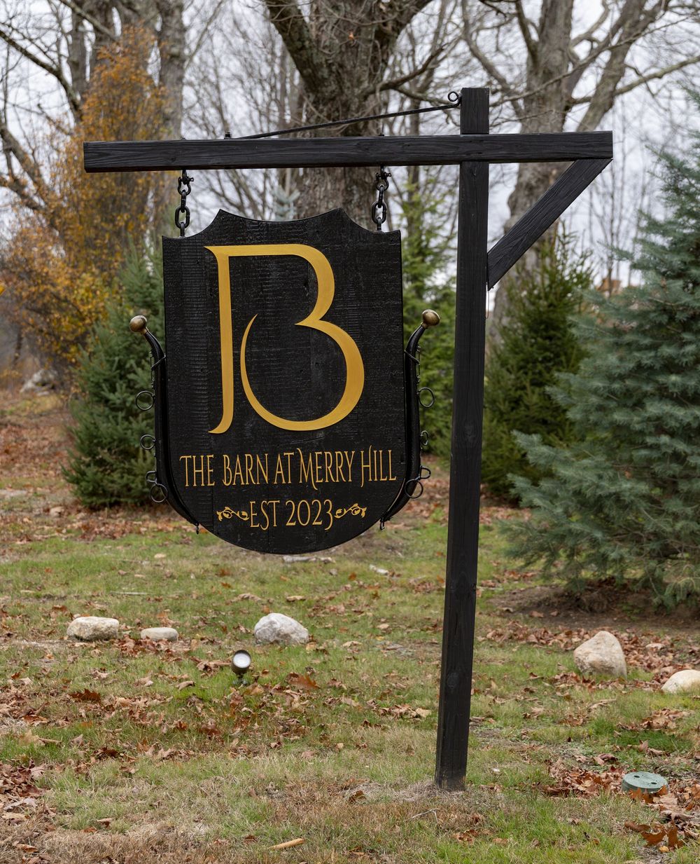 Series of black wooden signs with gold lettering displaying 'JB' mounted on posts in an autumn landscape.