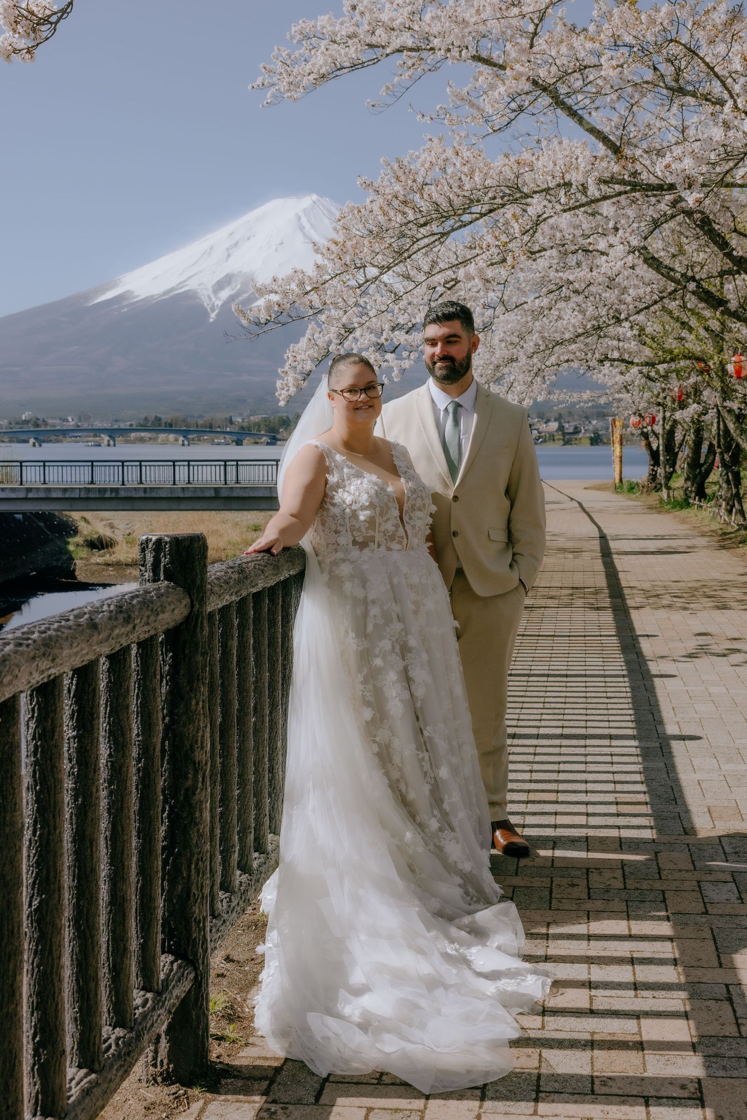 A couple poses under blooming cherry blossoms with Mount Fuji in the background during a spring wedding photo session.