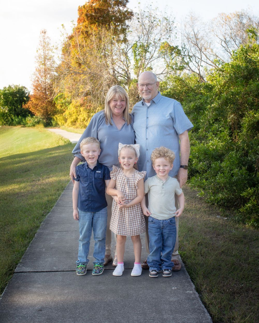 A family group poses together on a concrete path surrounded by autumn foliage and greenery.